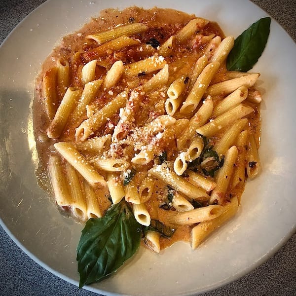 Penne pasta in a creamy tomato sauce with parmesan cheese and fresh basil on a white plate.