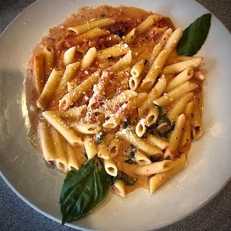Penne pasta in a creamy tomato sauce with parmesan cheese and fresh basil on a white plate.