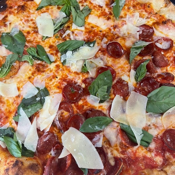 Close-up of a Soprano's Pizzeria pepperoni pizza with fresh basil and shaved Parmesan cheese.