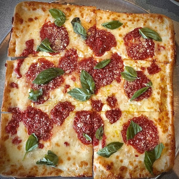 Square-cut Soprano's Pizzeria pizza with melted cheese, dollops of red sauce, and fresh basil leaves.