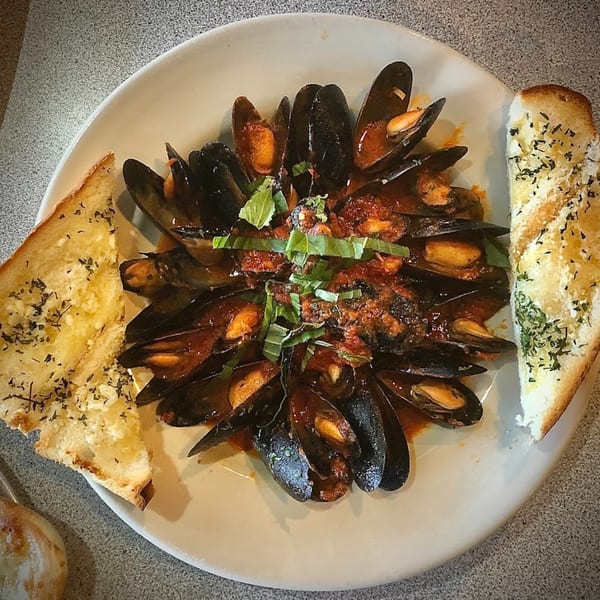 Mussels in red sauce with basil and two slices of garlic bread on a white plate.