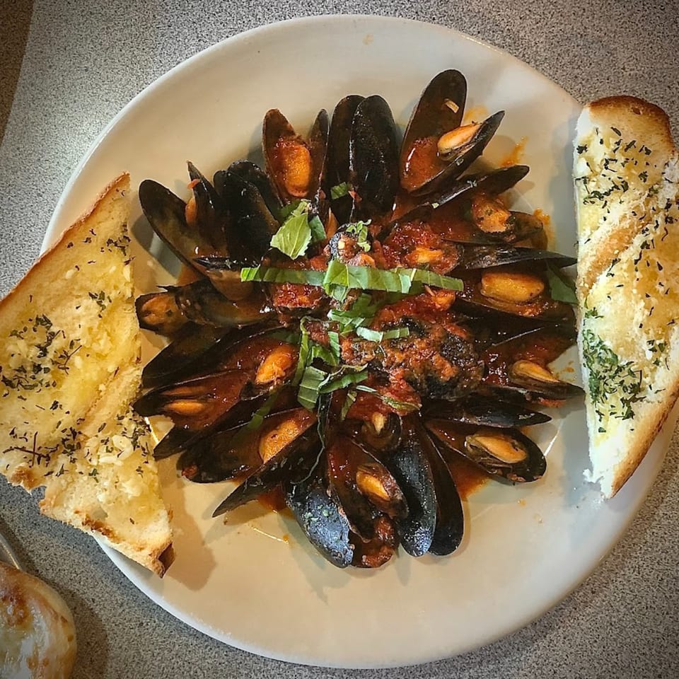 Mussels in red sauce with basil and two slices of garlic bread on a white plate.