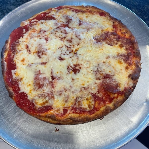 A whole Soprano's Pizzeria pepperoni pizza with melted cheese on a round metal tray.
