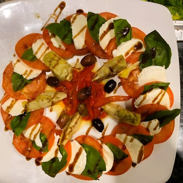 Caprese salad with tomatoes, mozzarella, basil, artichokes, olives, and balsamic glaze.