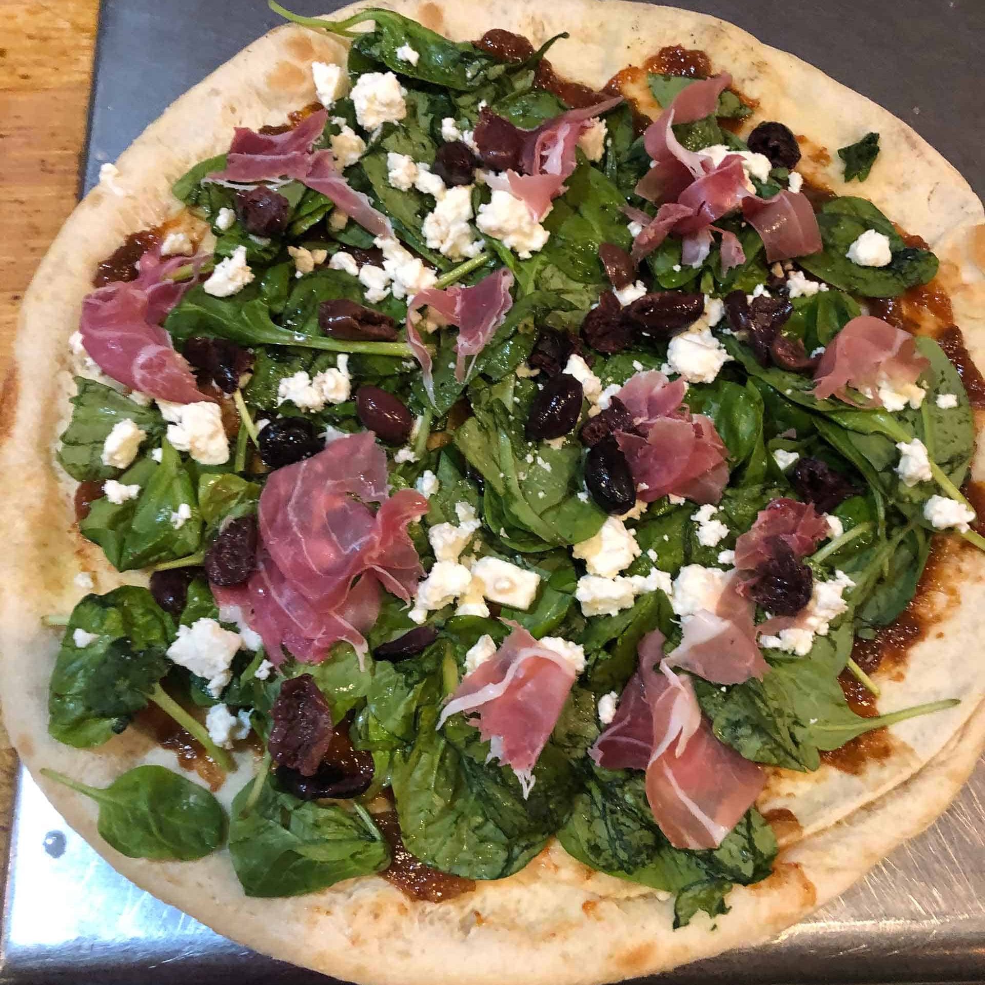 A pizza with spinach and ham on it.